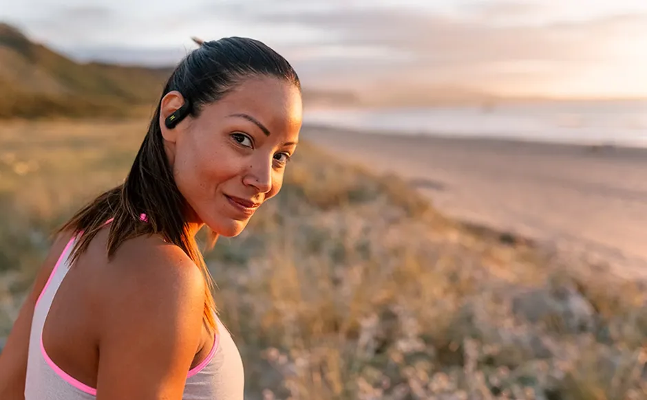 Donna in spiaggia al tramonto con JBL Endurance Peak 4
